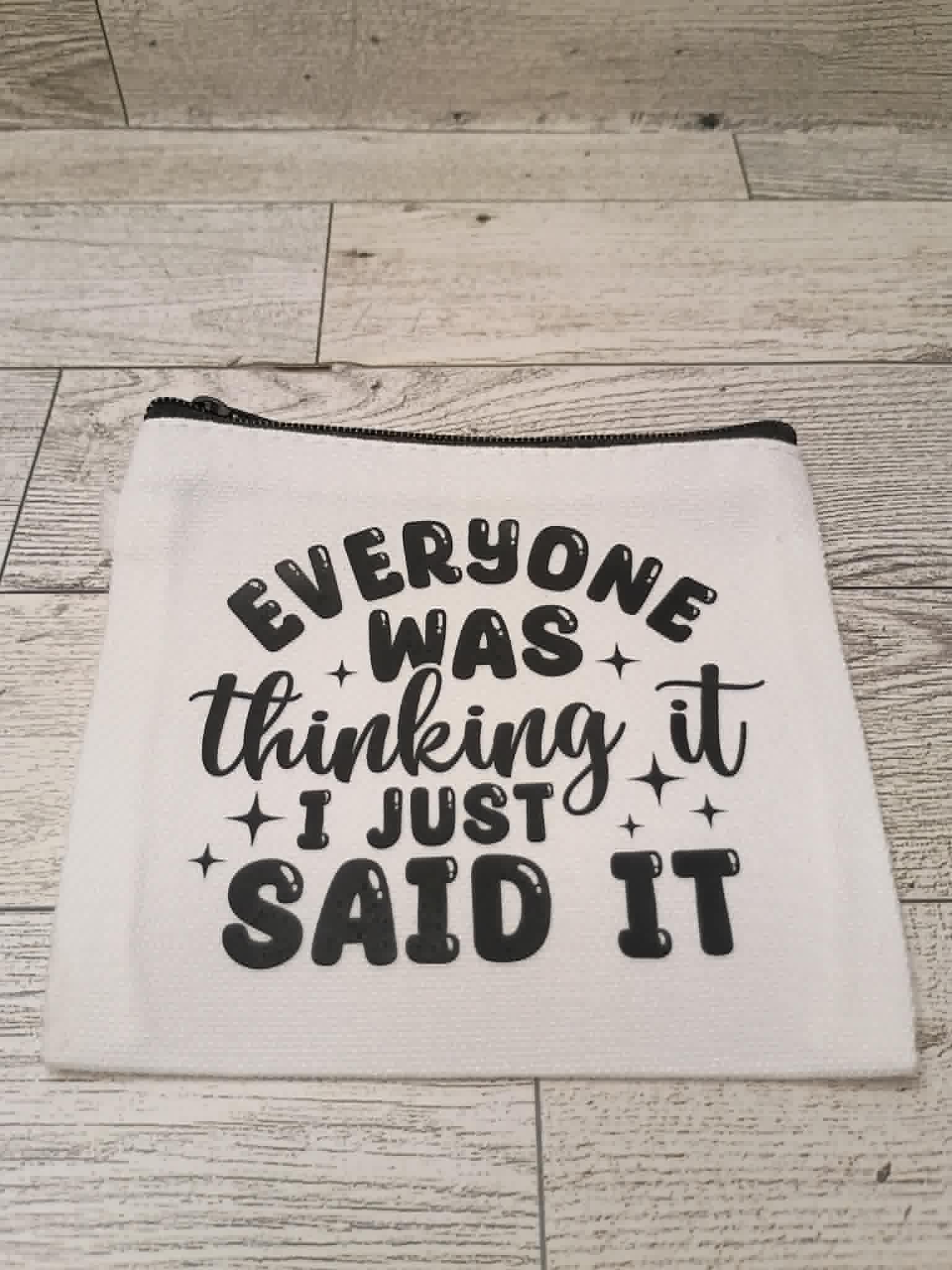 A white fabric zippered pouch with black text reading 'EVERYONE WAS thinking it I JUST SAID IT' and small star accents, placed on a light wood plank surface.