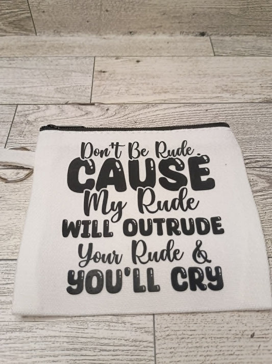 An off-white fabric pouch with a black zipper and black printed text that reads, 'Don't Be Rude. CAUSE My Rude WILL OUTRUDE Your Rude & YOU'LL CRY,' displayed on a light wood plank background.