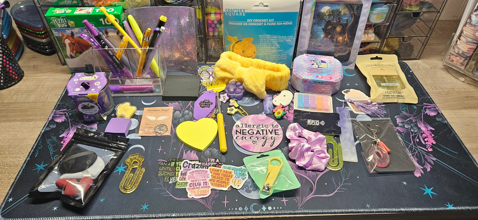 A large assortment of stationery and desk accessories laid out on a dark patterned mat, including pens, sticky notes, clips, a yellow plush item, packaged items, and small accessories, photographed in a retail or storage setting.