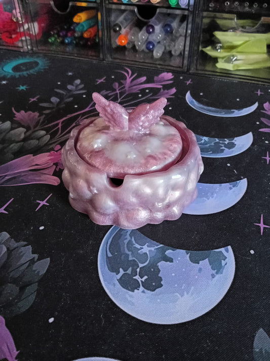 Pink ceramic teapot with butterfly wings on a dark surface with moon and star designs.