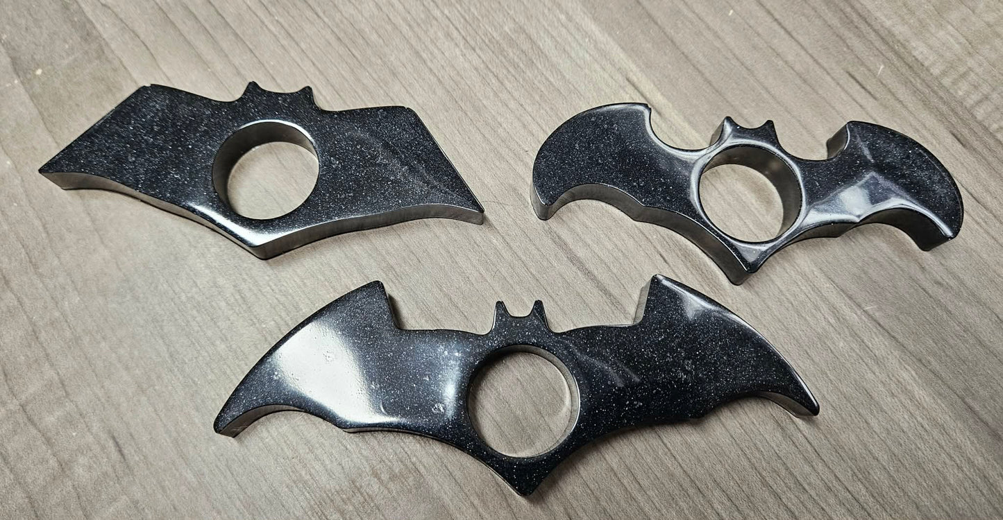 Three bat-shaped knuckle dusters on a wooden surface