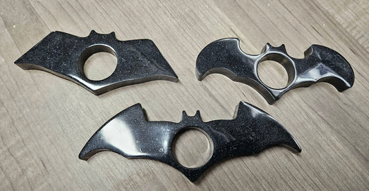 Three bat-shaped knuckle dusters on a wooden surface