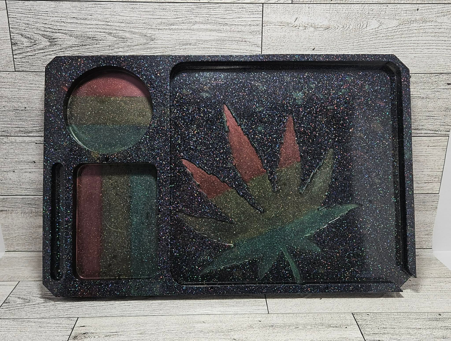 Black textured tray with circular and leaf-shaped compartments on a wooden surface