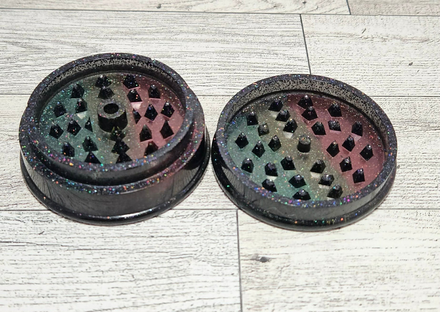 Two black  patterned grinders on a light wooden surface