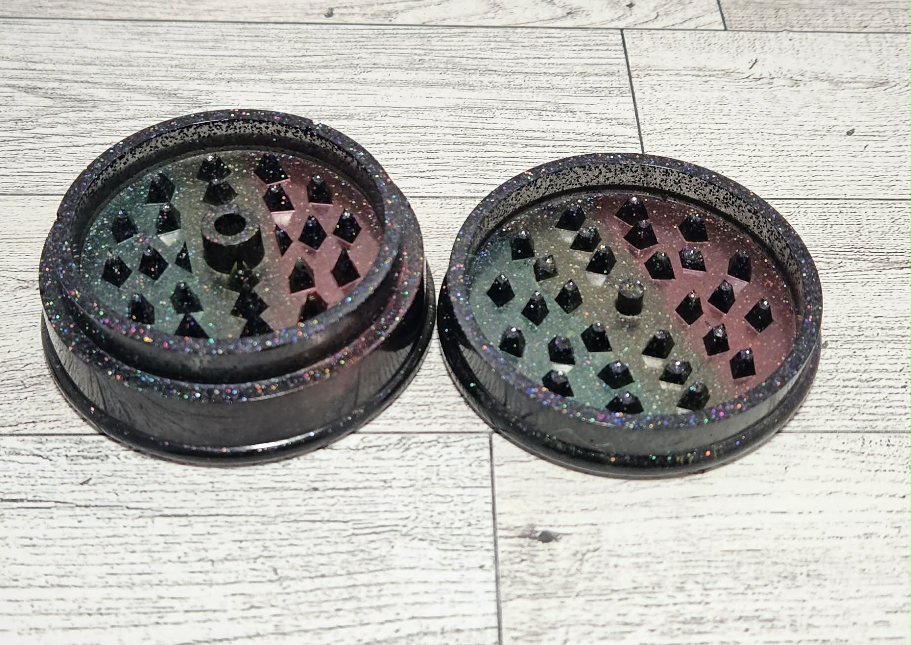 Two black  patterned grinders on a light wooden surface