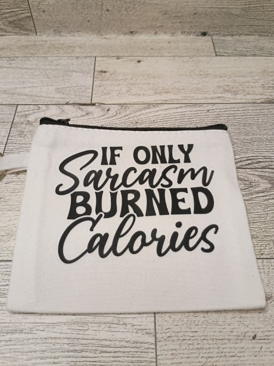 A white fabric zippered pouch with black text reading 'IF ONLY Sarcasm BURNED Calories' laid flat on a light wood plank surface.