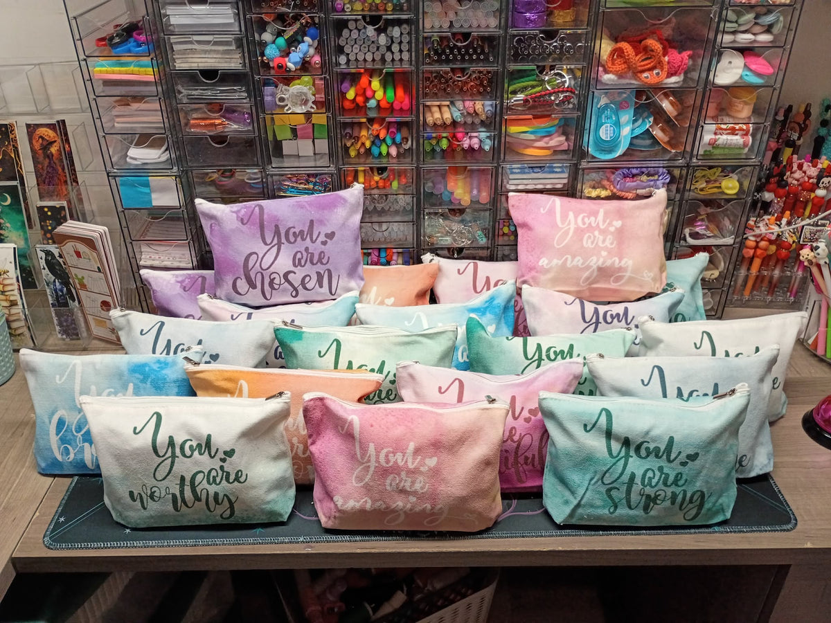 A collection of pastel-colored throw pillows with embroidered motivational phrases like 'You are chosen', 'You are amazing', and 'You are worthy', displayed on a table in a craft supply store.