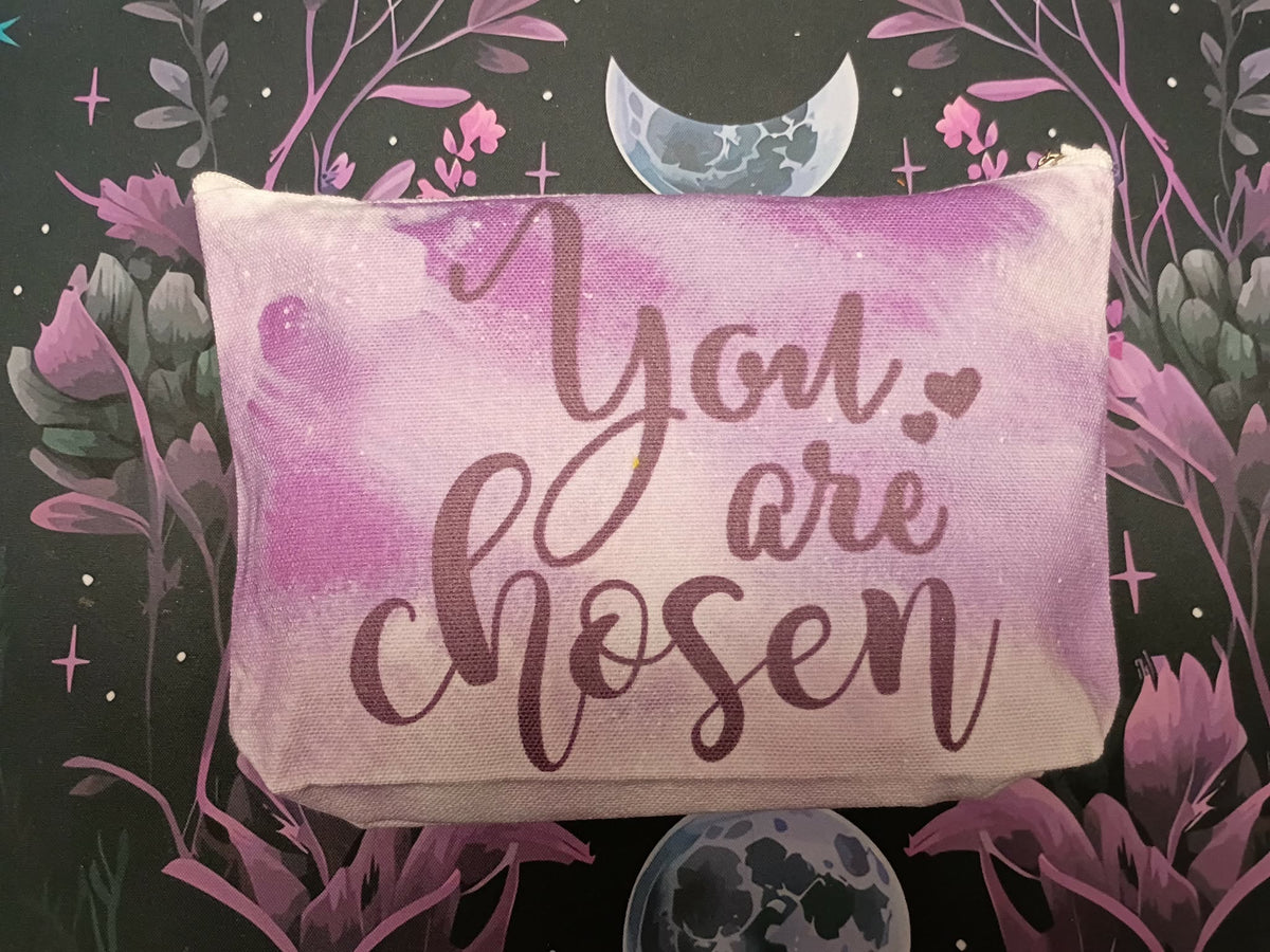 A rectangular decorative pillow with a pink and purple watercolor design and the phrase 'You are chosen' in dark purple script, set against a dark background with floral and moon illustrations.